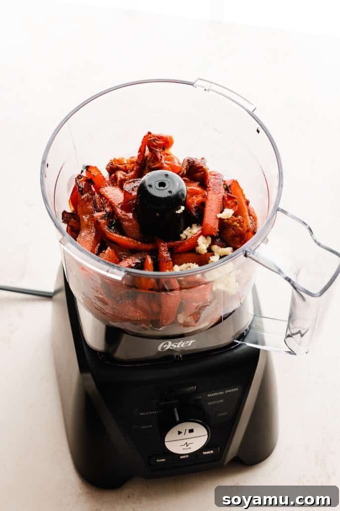 Roasted red peppers, fresh garlic, and basil being added to a food processor, signaling the start of blending the creamy sauce.