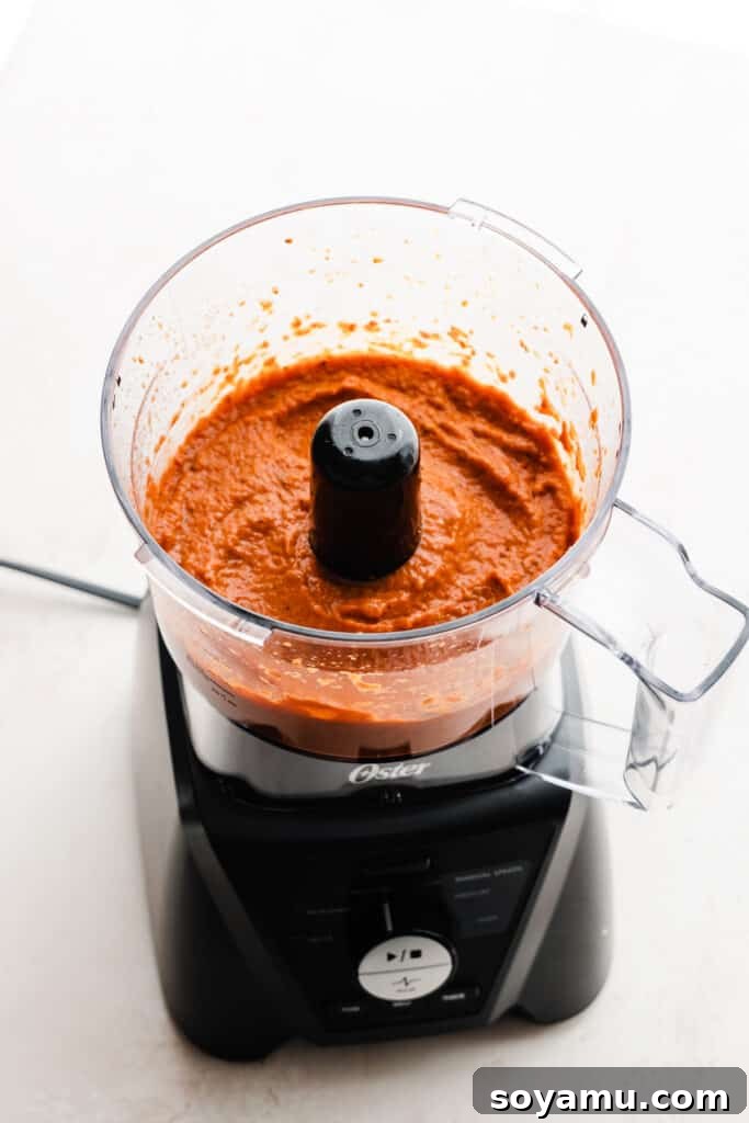A perfectly smooth and creamy roasted red pepper sauce blended in a food processor, highlighting its luscious texture and vibrant color.