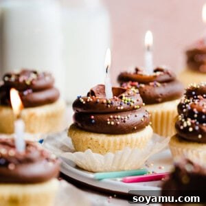 Yellow birthday cupcakes with chocolate frosting and rainbow sprinkles with lit birthday candles.