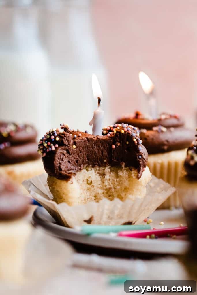 A close-up view of a perfectly frosted yellow cupcake with a bite missing, showcasing its moist texture and rich chocolate malt frosting.