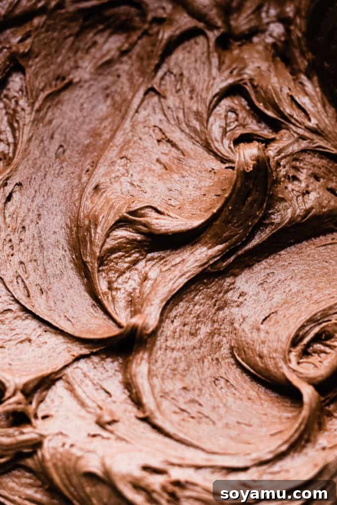 A close-up of elegantly swirled, silky chocolate frosting on top of a cupcake, ready for sprinkles.