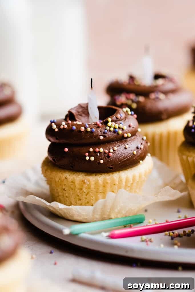 A tantalizing close-up of a birthday cupcake featuring perfect swirls of malted chocolate frosting, vibrant colorful sprinkles, and a warm, inviting glow.