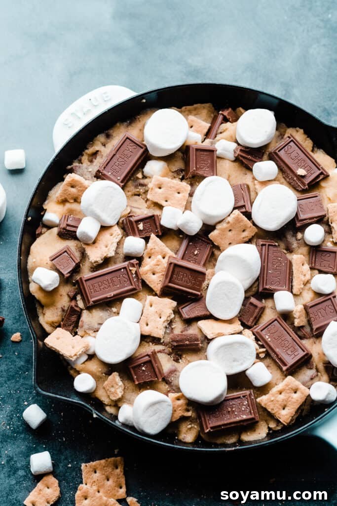 Gooey S'mores Skillet Cookie 7 The unbaked s'mores skillet cookie, lavishly topped with marshmallows, graham crackers, and chocolate pieces, ready for the oven.