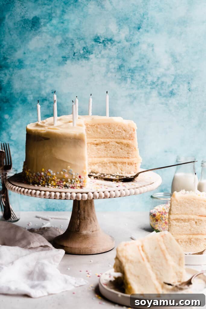 Pristine White Birthday Masterpiece 2 The sliced three-layer white cake decorated with pastel sprinkles and birthday candles, with a blue background, showcasing its perfect crumb and inviting presentation.