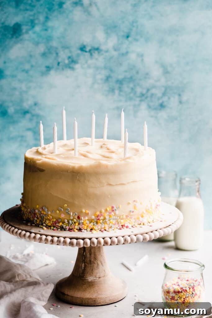 Pristine White Birthday Masterpiece 9 The uncut white cake, elegantly decorated with pastel sprinkles, presented on a pristine cake stand against a soft blue backdrop.