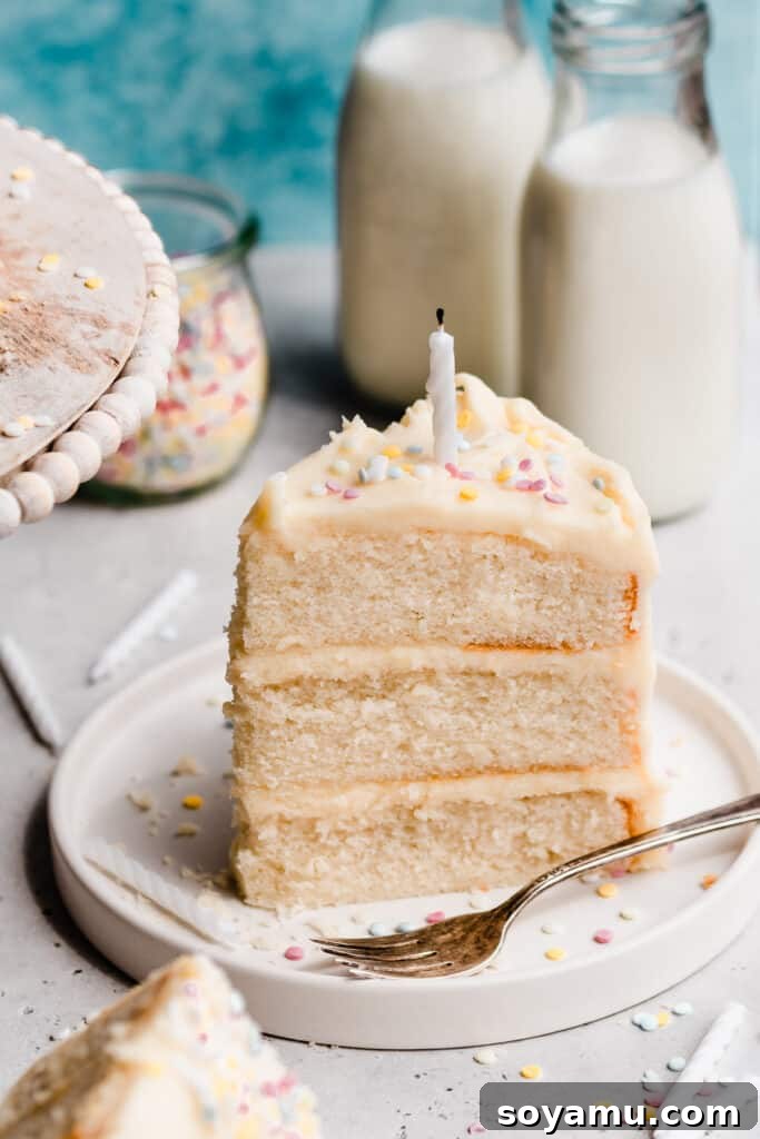 Pristine White Birthday Masterpiece 10 A 3/4 angle shot of a slice of white cake on a plate, adorned with a festive birthday candle and colorful sprinkles on top.