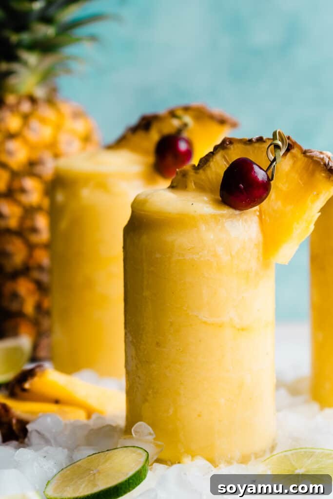 Paradise Frost 2 A close-up on a glass of bright yellow pineapple piña colada with a wedge of pineapple and cherry on top, evoking a tropical vibe.