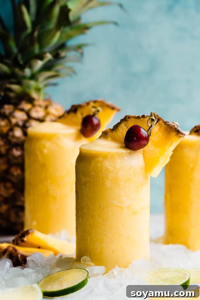 Paradise Frost 3 Three glasses of frozen pineapple piña coladas against a bright blue backdrop, ready for a summer party.