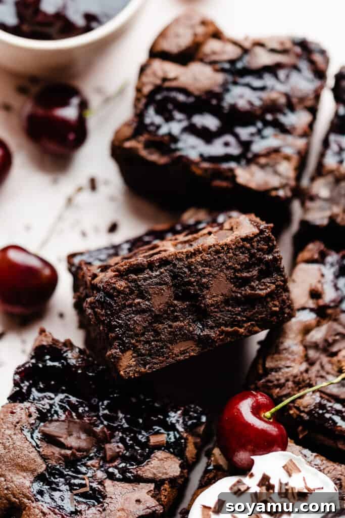 A close-up shot revealing the rich, fudgy interior of a perfectly baked Black Forest Brownie, showcasing visible swirls of deep red cherry sauce and luscious melted chocolate chunks. This image emphasizes the moist, dense, and truly decadent texture of the dessert.