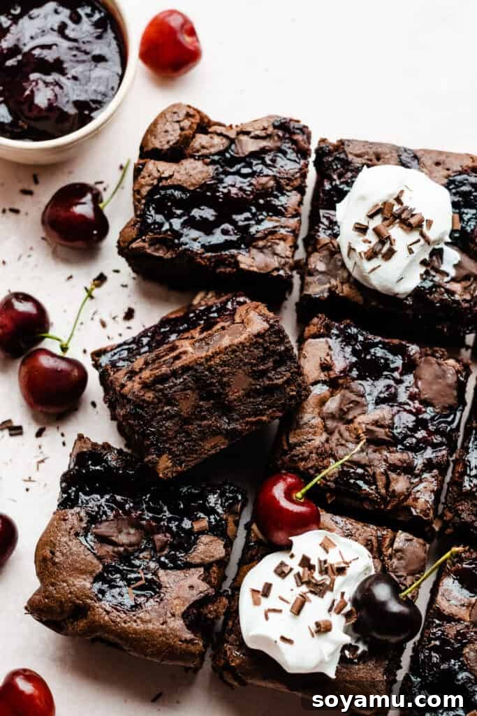A selection of individually sliced Black Forest Brownies, elegantly arranged and garnished. Each brownie is topped with a generous dollop of fluffy whipped cream, fresh, vibrant red cherries, and delicate chocolate shavings, highlighting their luxurious dessert appeal and inviting indulgence.