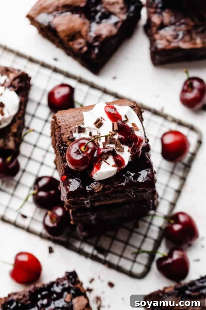 A stunning bird's eye view of a stack of luxurious Black Forest Brownies, generously adorned with fluffy whipped cream and vibrant cherry sauce. Fresh, ripe cherries are artfully scattered around the dessert, emphasizing its freshness, natural ingredients, and irresistible visual appeal.