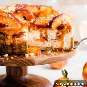 The peach cobbler cheesecake on a cake stand with a cross section cut. Juicy peach slices are on top with cinnamon peach juice dripping down.