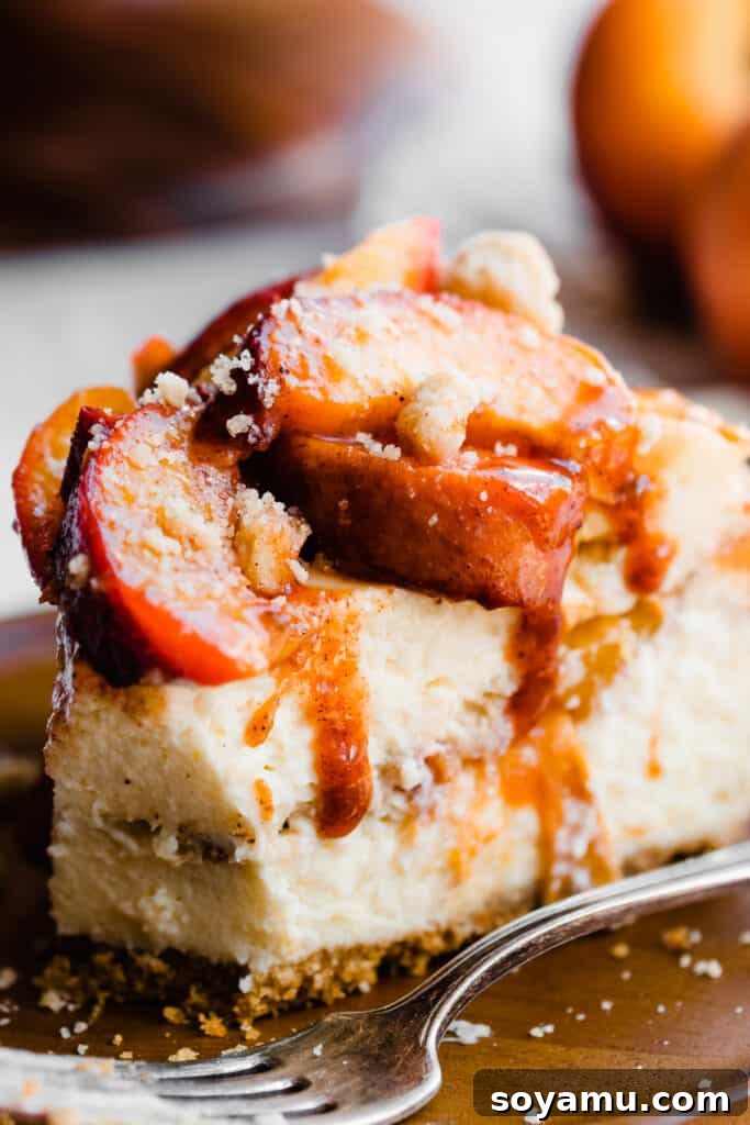 A close-up of a perfectly cut slice of the peach cobbler cheesecake, with fresh juicy peaches on top and delightful peach juice gently dripping down the sides.