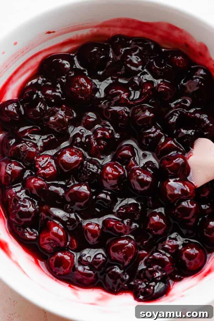 Effortless Black Forest Bliss 4 A vibrant bowl of homemade cherry sauce, featuring whole and halved dark cherries in a thick, glossy, kirsch-infused compote.