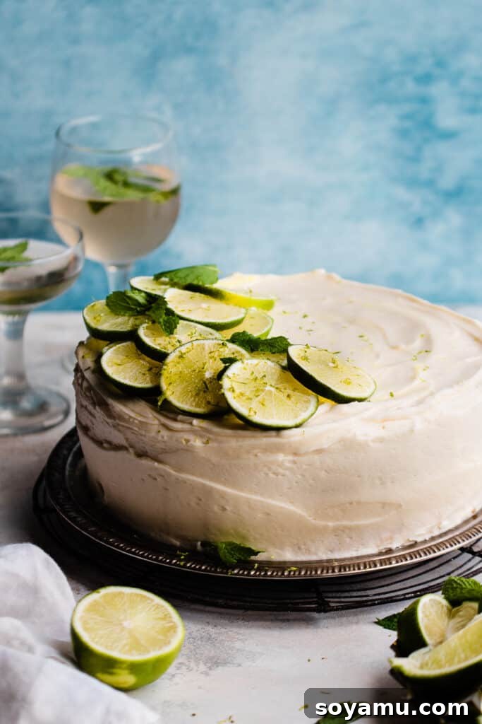 Zesty Mojito Cake with Spiked Rum Buttercream 9 The Lime Cake on a cake plate with fresh limes and mint on top, against a blue backdrop, ready to be served.