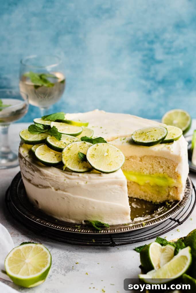 Zesty Mojito Cake with Spiked Rum Buttercream 10 A sliced lime cake topped with fresh lime slices and mint, on a blue backdrop, showing the beautiful cross-section.
