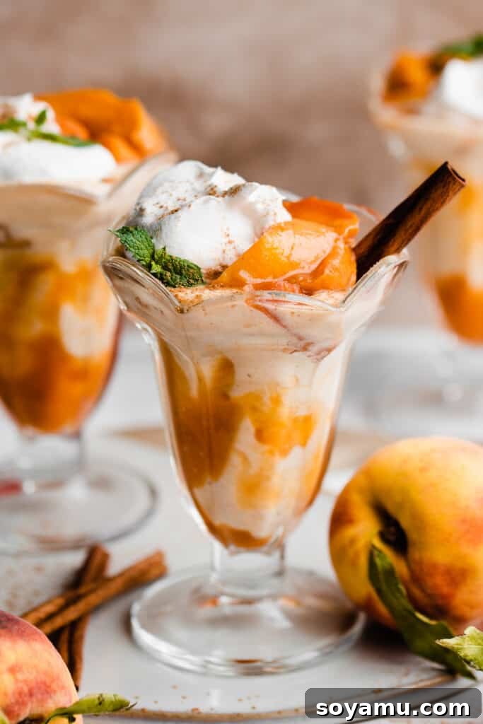 Swirled Homemade Peach Pie Milkshake 7 A close-up of a beautifully presented peach milkshake in an old-fashioned glass, lavishly adorned with fresh peach chunks, a swirl of whipped cream, and an aromatic cinnamon stick for garnish.