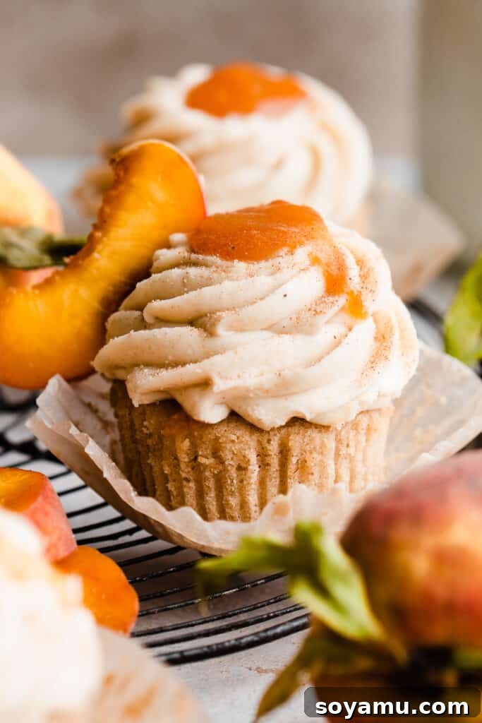 Luscious Peach Cupcakes Crowned with Cinnamon Cream Cheese Frosting 11 A close-up shot of a single peach cupcake, beautifully frosted with cinnamon cream cheese and topped with peach filling, on a white plate.