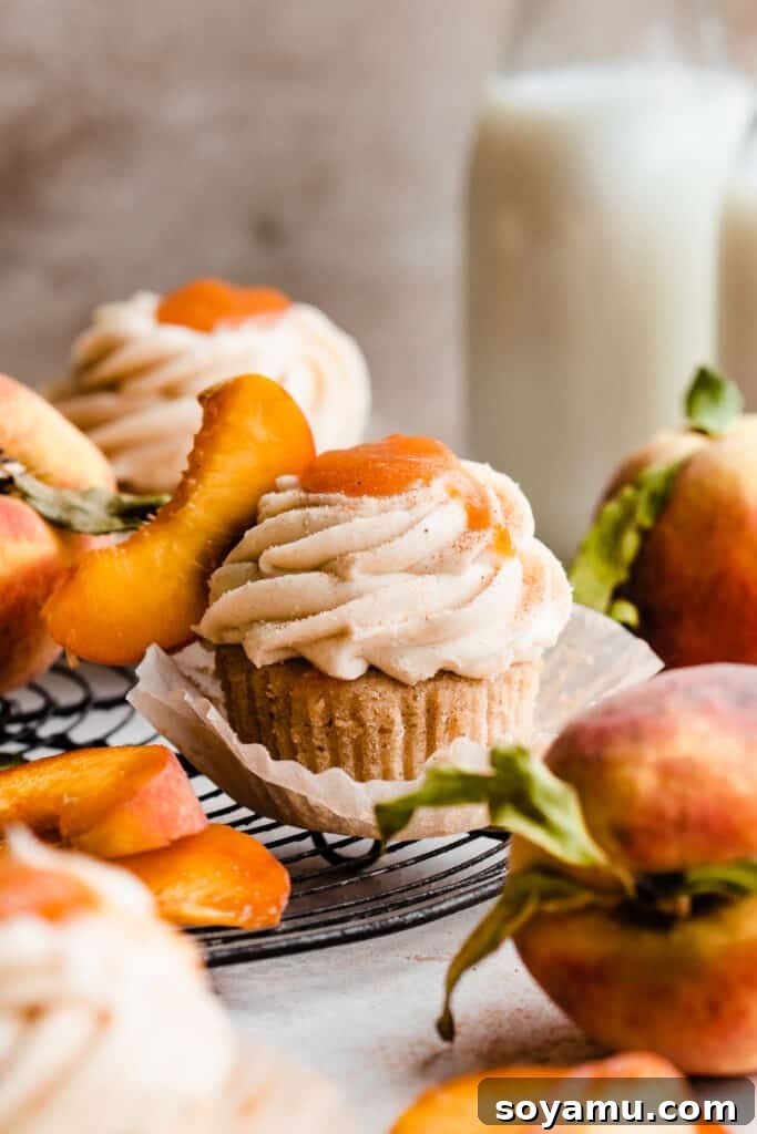Luscious Peach Cupcakes Crowned with Cinnamon Cream Cheese Frosting 12 A collection of peach cupcakes arranged on a vintage wire rack, garnished with cinnamon cream cheese frosting, peach filling, and fresh peach slices.
