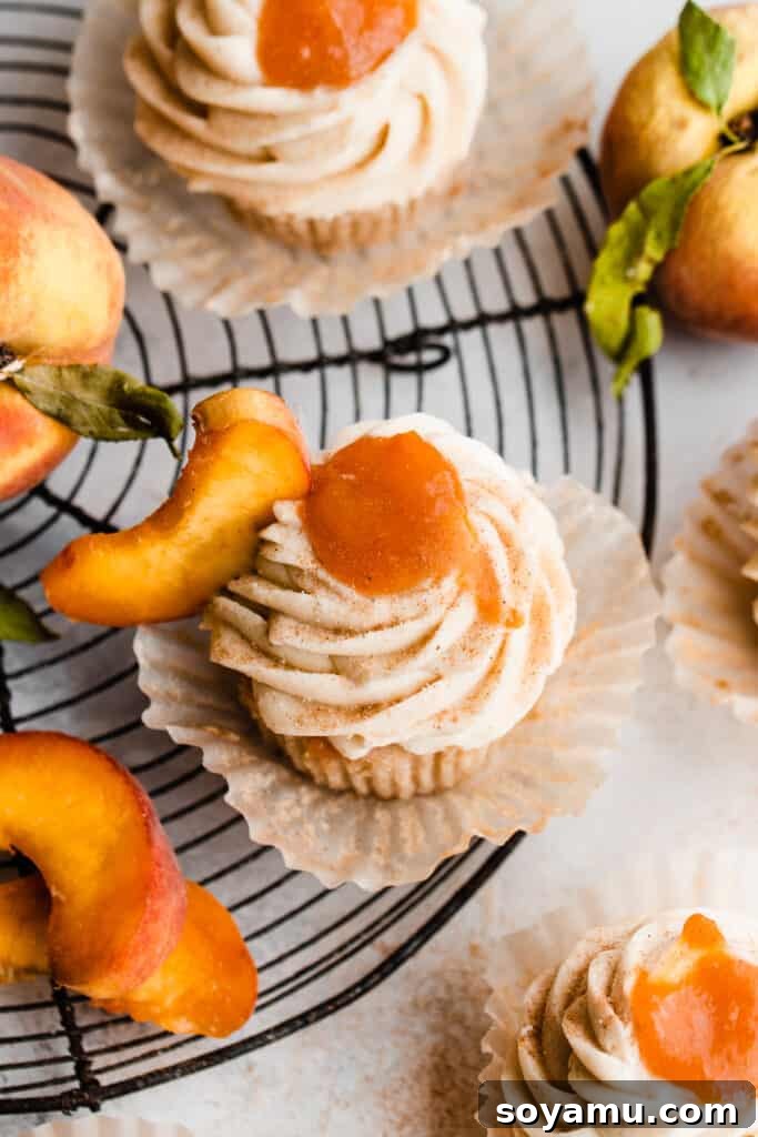Luscious Peach Cupcakes Crowned with Cinnamon Cream Cheese Frosting 3 A birds eye view of several peach pie cupcakes arranged on a wire rack, showcasing their elegant frosting and dollops of peach filling.