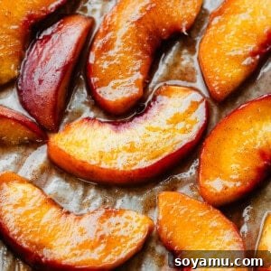 A close-up of juicy roasted peach slices on a baking sheet, ready for serving.
