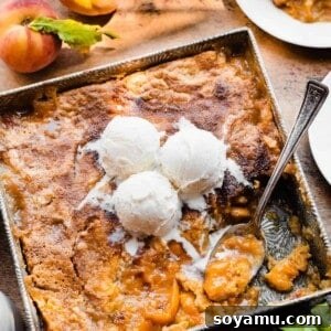 Cake mix peach cobbler in a baking dish with vanilla ice cream on top.