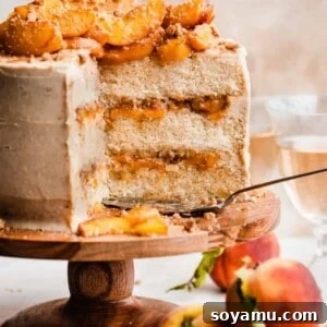 Golden Peach Cobbler Cake with Nutty Brown Butter Frosting 14 A sliced peach cobbler cake on a cake stand with visible layers of brown butter frosting, peach filling, and streusel.