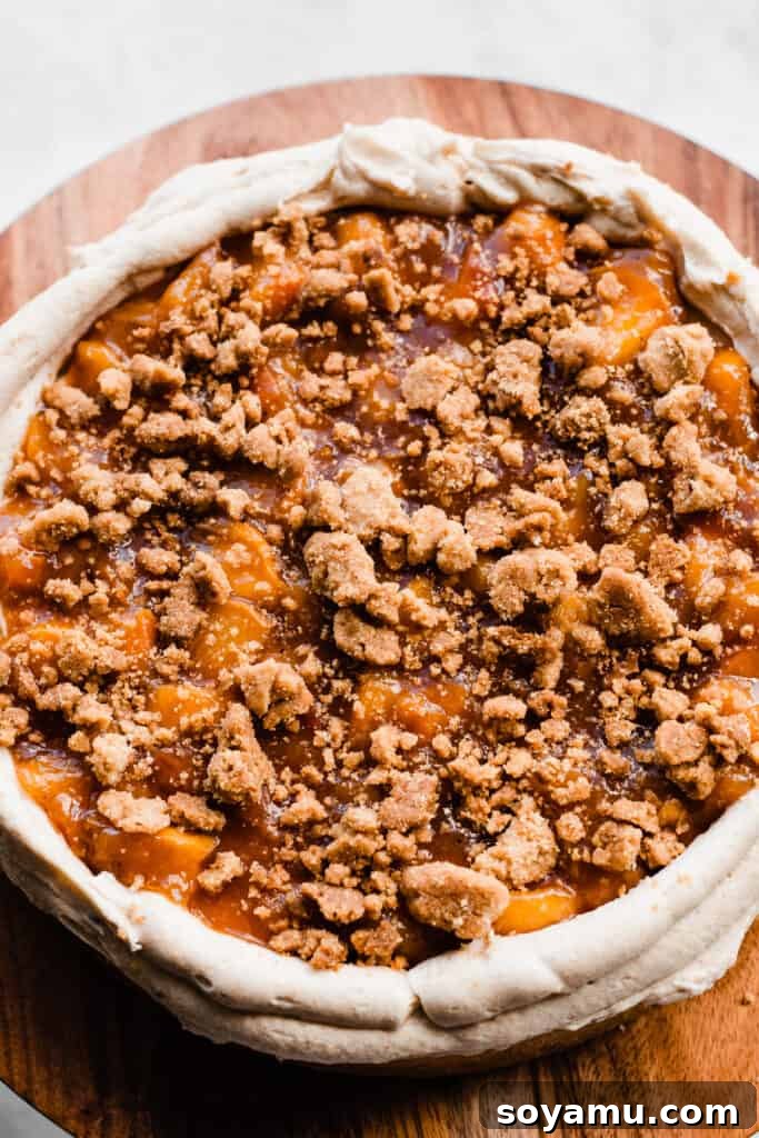 Golden Peach Cobbler Cake with Nutty Brown Butter Frosting 9 A close-up view of a cake layer topped with brown butter frosting, vibrant peach filling, and crunchy streusel, ready for the next layer.