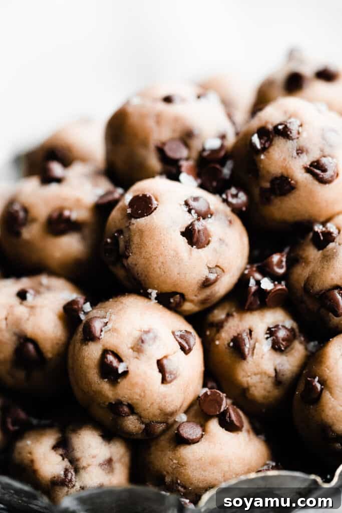 No-Bake Cookie Dough Poppers 9 A close-up of a pile of edible cookie dough balls, beautifully sprinkled with extra mini chocolate chips and delicate flaky sea salt.