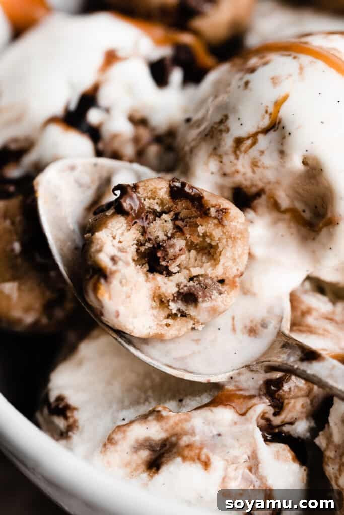 No-Bake Cookie Dough Poppers 10 A spoon holding an edible cookie dough bite, with a small bite taken out, resting in a bowl of ice cream.