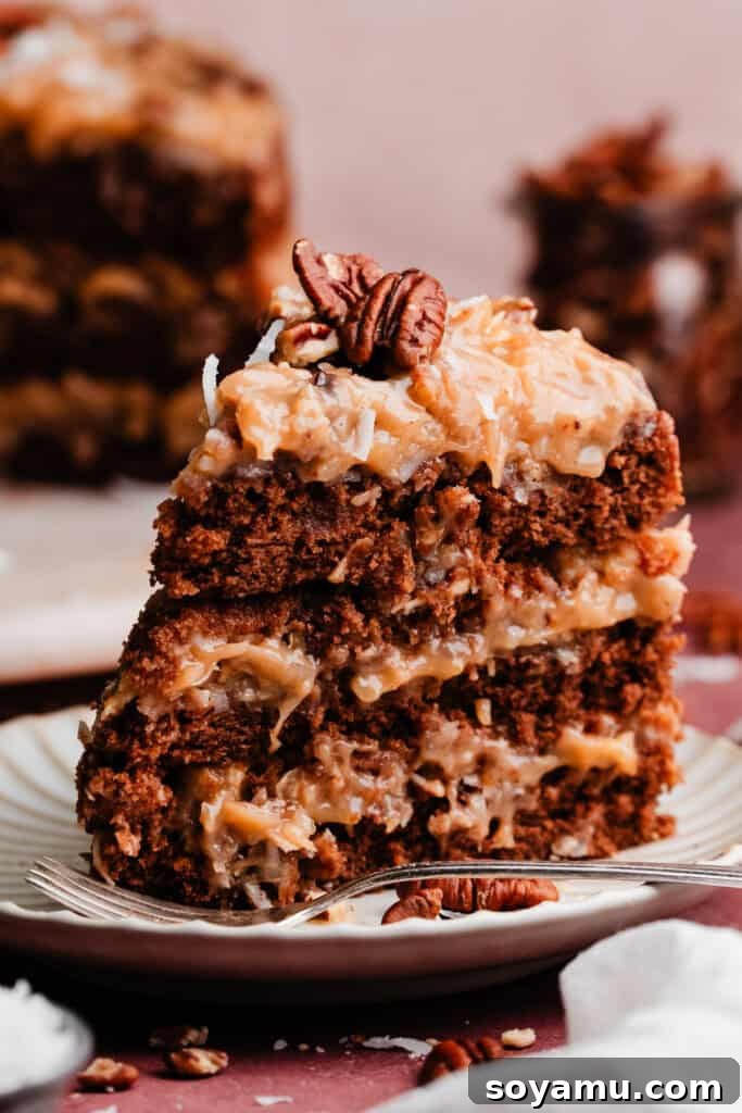 A single, perfectly cut slice of German Chocolate Cake stands tall on a marble cake plate, showcasing its layers and rich frosting.