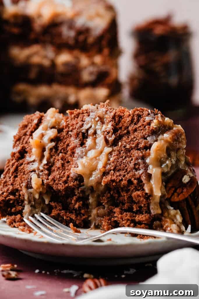 A close-up view of a slice of German Chocolate Cake, showing off the fluffy chocolate layers and thick, gooey coconut pecan frosting with a few bites taken out.