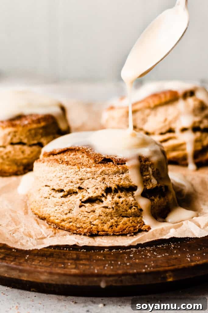 Warm Maple Biscuits with a Velvety Maple Glaze 2 Three tall maple biscuits being drizzled with maple glaze, showcasing their flaky layers and golden-brown tops.