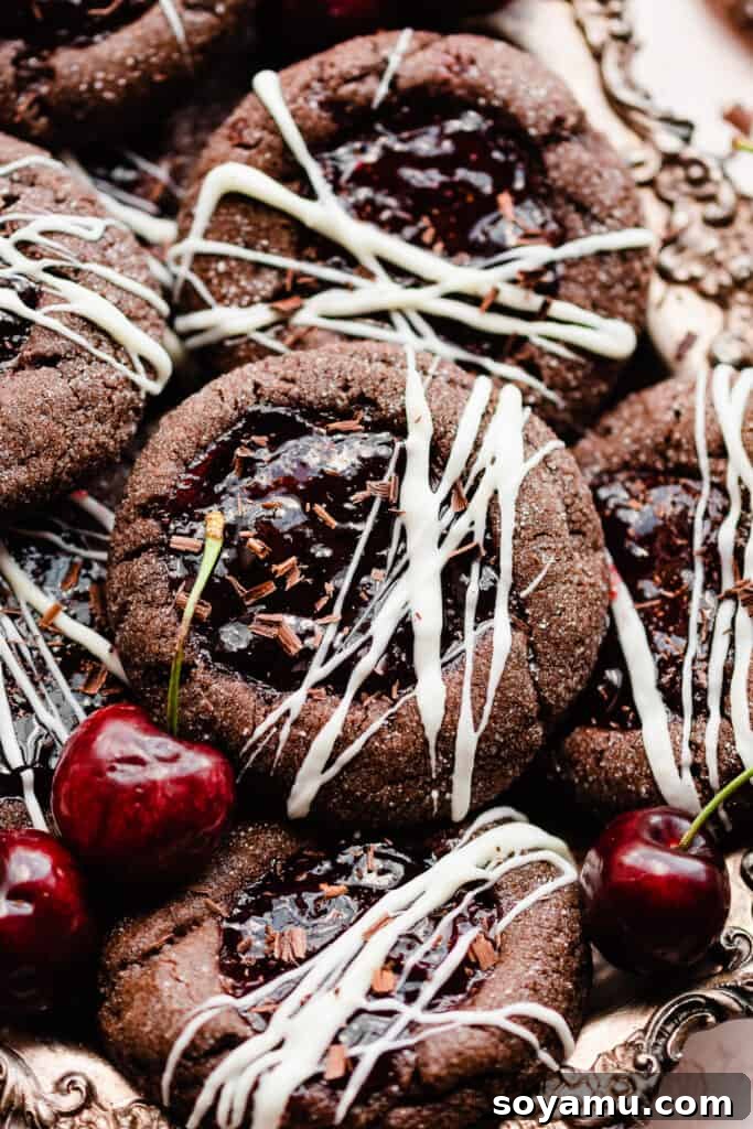 Midnight Forest Cherry Cookies 7 A close-up shot of a single Black Forest Cookie, placed atop a pile of others, with fresh cherries artfully scattered around, emphasizing its rich texture and appealing presentation.