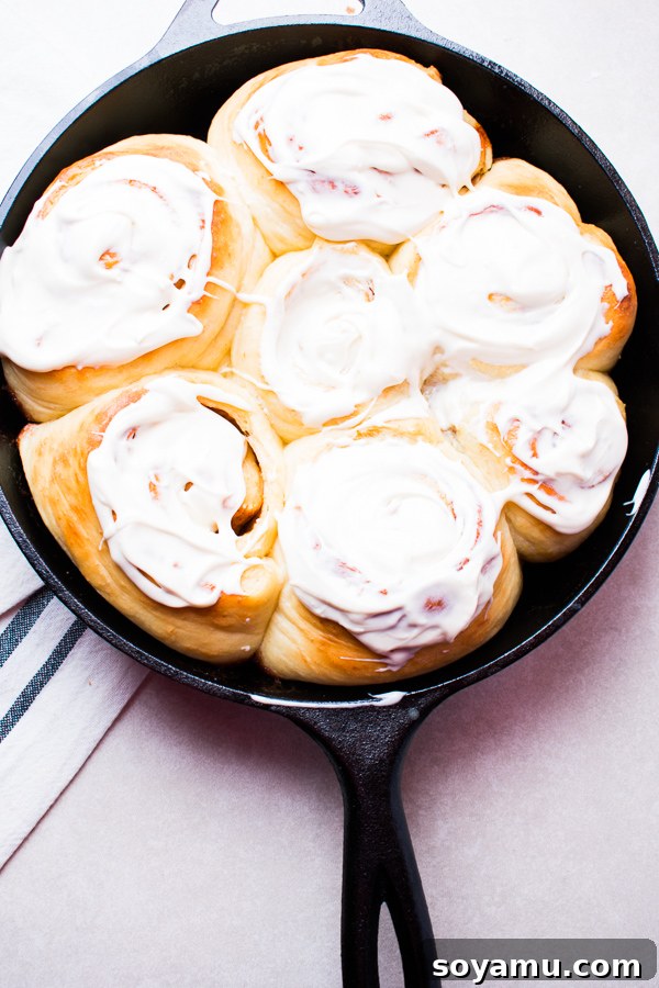 Freshly baked cast iron cinnamon rolls, golden brown and covered in cream cheese frosting.