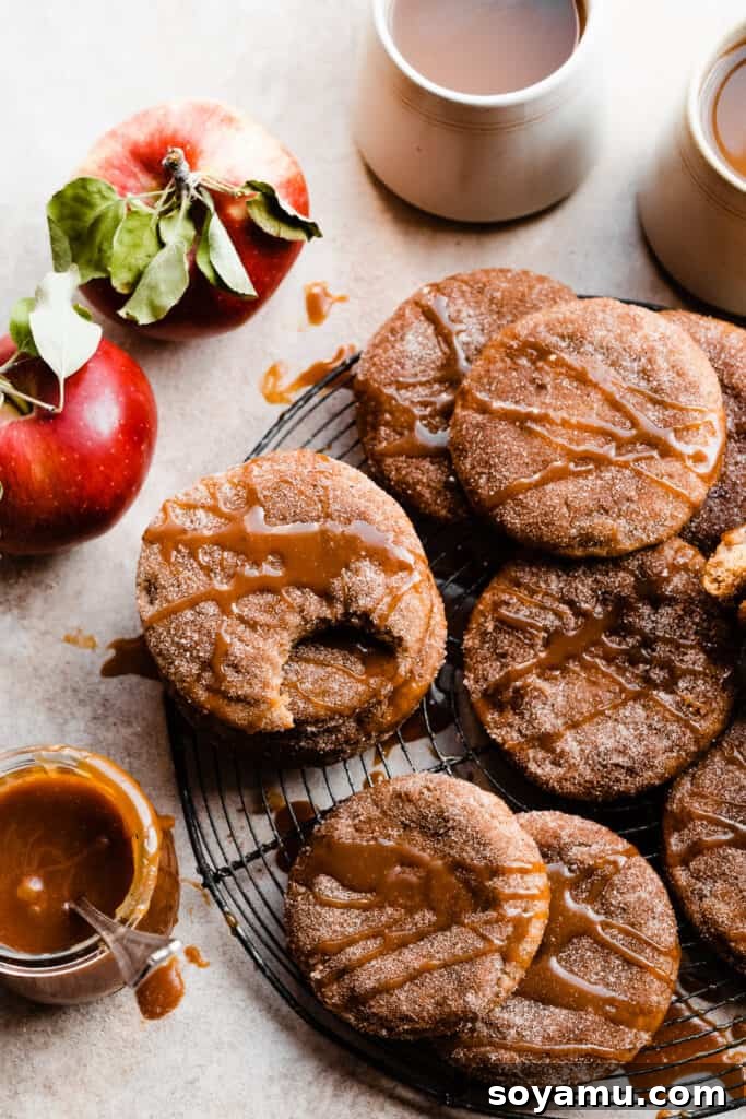Spiced Caramel Apple Cider Cookies 8 Beautifully styled Caramel Apple Cider Cookies on a wire rack, drizzled with caramel, surrounded by vibrant red apples and mugs of steaming cider – an idyllic fall scene.