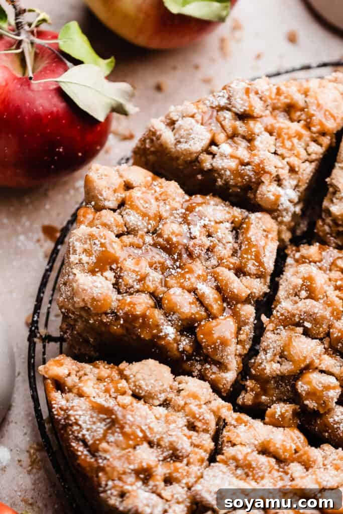 A close-up on slices of the caramel apple crumb cake on a wire rack, with leafy apples nearby, highlighting the rustic autumn aesthetic.