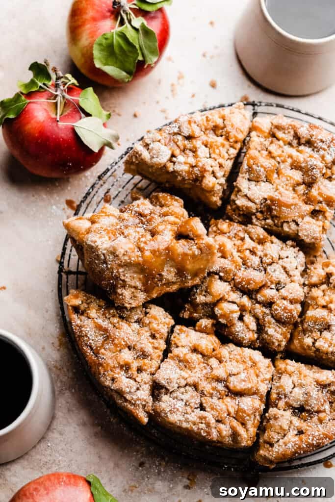 The sliced caramel apple crumb cake on a wire rack, with leafy apples and mugs of coffee nearby, creating a warm and inviting scene.