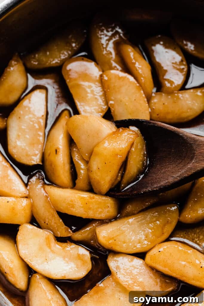 A close-up of caramelized apple slices glistening in a pan, infused with spices.