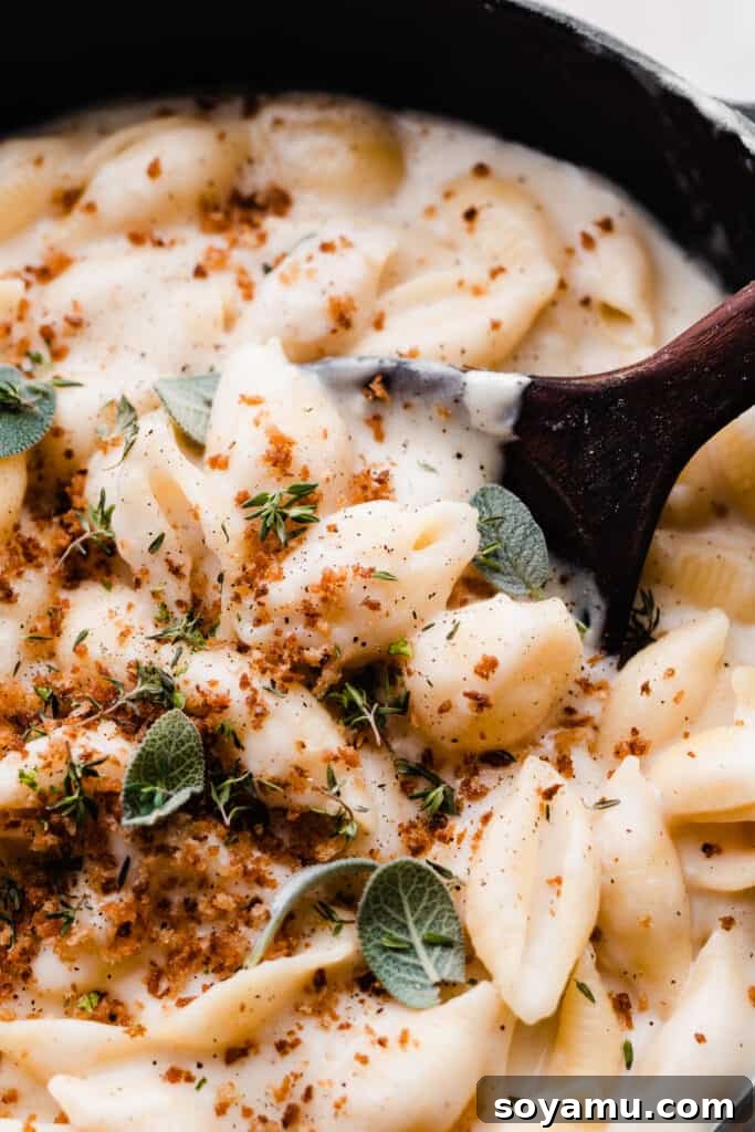 Creamy White Cheddar Mac with Crispy Brown Butter Crumbs 2 A close-up of a pot of creamy white cheddar mac and cheese with a serving spoon digging in, revealing the rich texture.