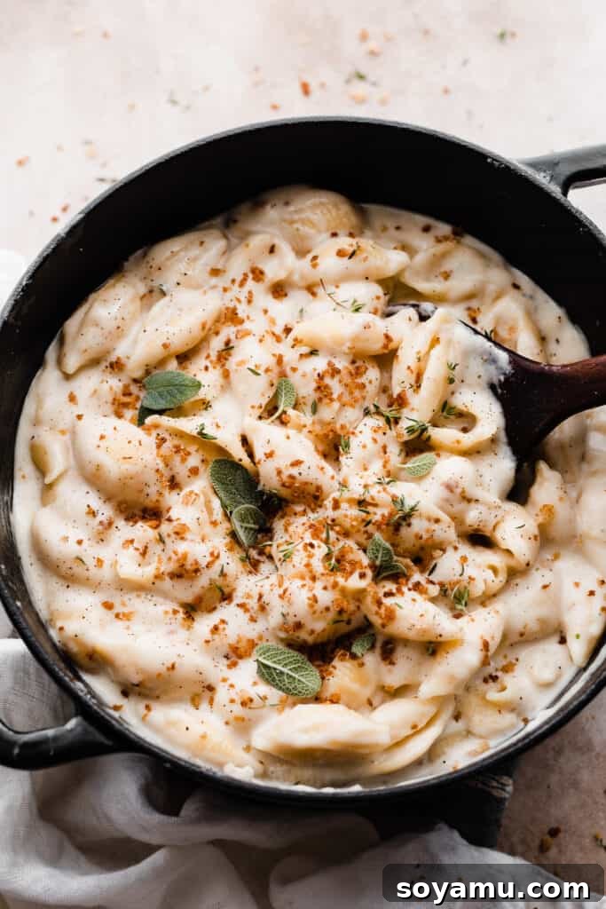 Creamy White Cheddar Mac with Crispy Brown Butter Crumbs 8 A pot of creamy white cheddar mac and cheese, beautifully topped with golden brown butter breadcrumbs, fresh sage, and thyme, with a wooden serving spoon ready to scoop.
