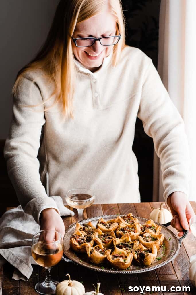 A close-up photo of the author lifting the tray of freshly baked lamb appetizer cups from a wooden tabletop, ready to serve.