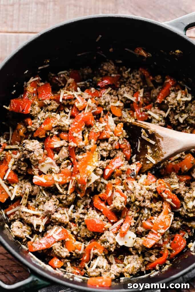 A Dutch oven filled with the rich, colorful appetizer mixture: seasoned lamb, roasted red peppers, pesto, and parmesan.