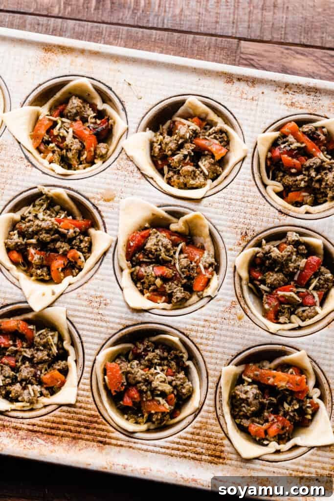 Unbaked lamb appetizer cups neatly arranged in a muffin tin, ready to be brushed with egg wash and baked.