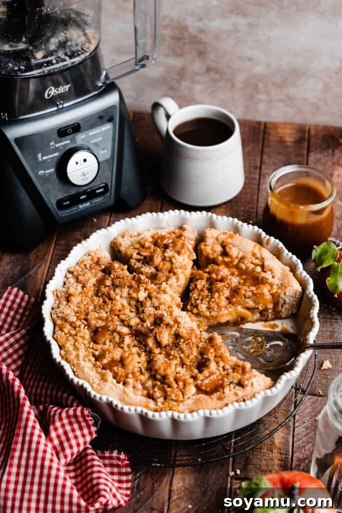 Decadent Caramel Apple Streusel Pizza 9 The apple dessert pizza in a pie plate, accompanied by cozy cups of coffee, highlighting its perfect pairing for a warm beverage.