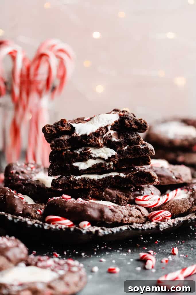 A straight-on view of a stack of broken open hot cocoa cookies, featuring the melty marshmallow and rich chocolate, with festive twinkle lights and candy canes in the blurred background.