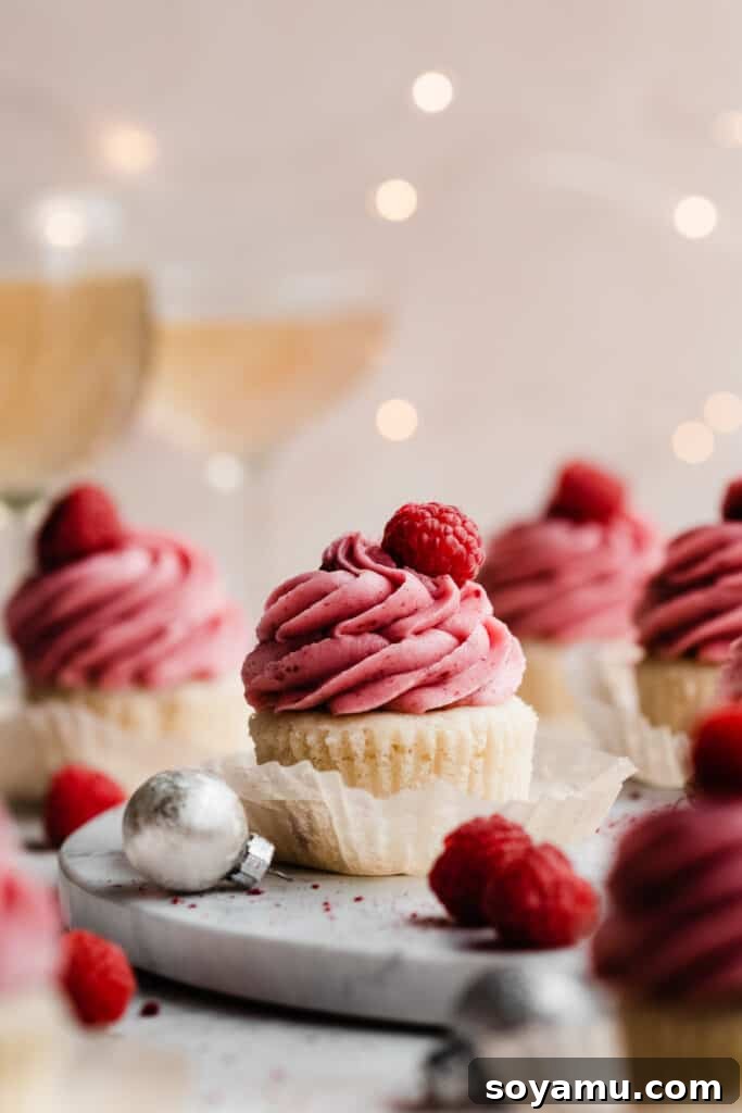 Pink Champagne Raspberry Delights 9 A collection of raspberry frosted cupcakes on a elegant marble surface, adorned with twinkling lights for a festive mood.