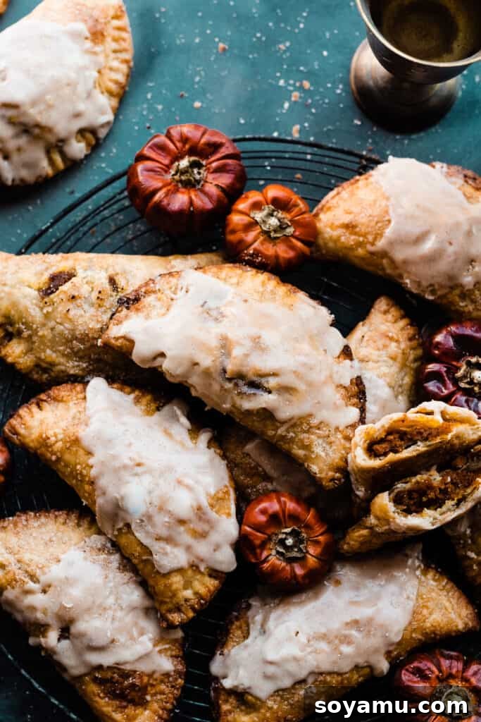 Golden Maple Glazed Pumpkin Pasties 7 Pumpkin pasties topped with maple glaze on a wire rack with small decorative pumpkins scattered around, creating an autumnal scene.
