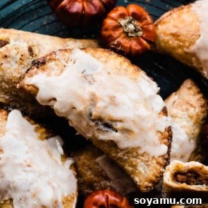 Pumpkin pasties glazed on a wire rack with mini pumpkins around.