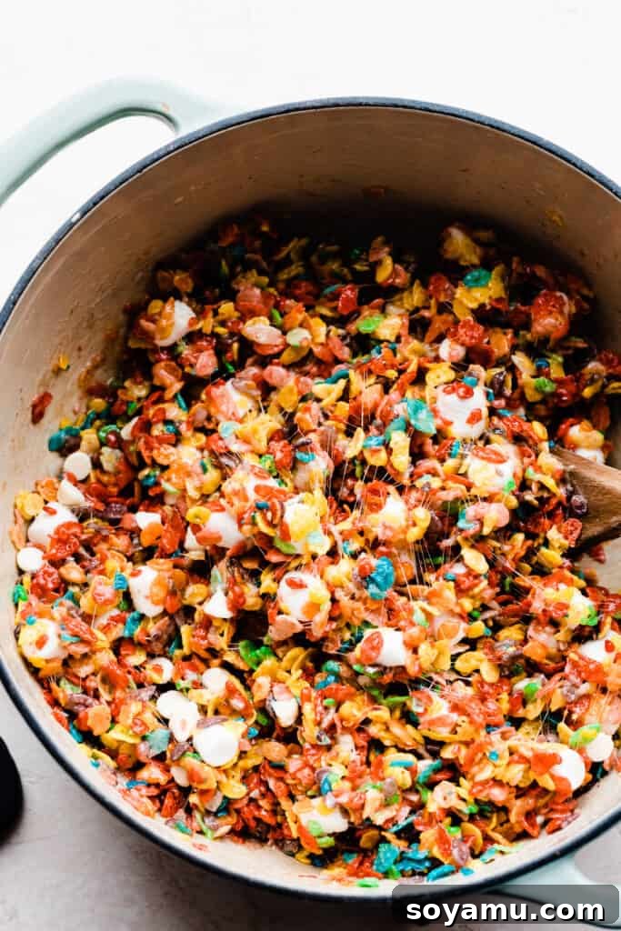 A Dutch oven filled with the colorful Fruity Pebbles cereal mixture, ready to be pressed into a pan.